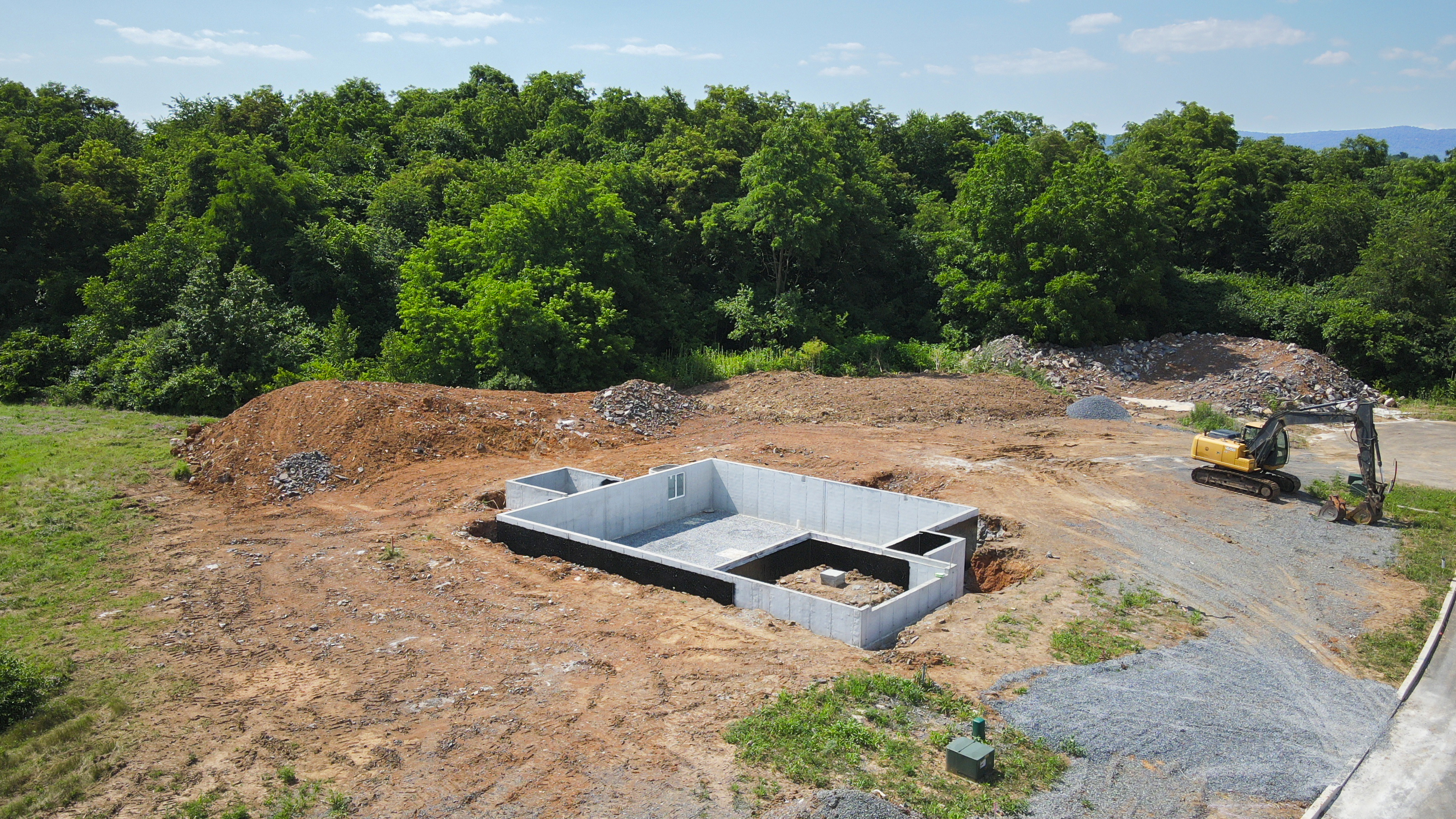 Stage 1 - Foundation.jpg: Excavated homesite with poured concrete foundation walls, gravel base, and prepared lot ready for framing to begin.
