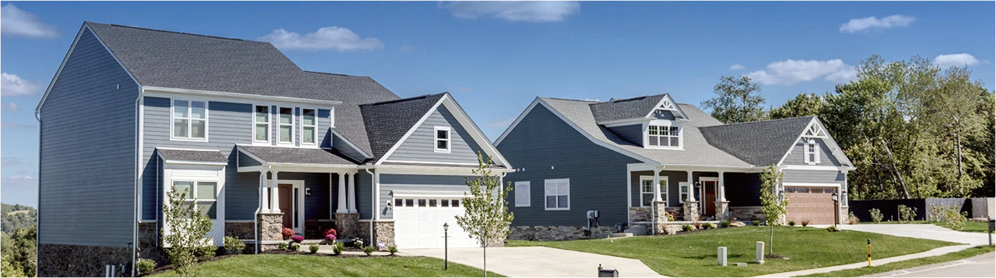 Two newly built homes with green grass on their lawns and a very blue sky